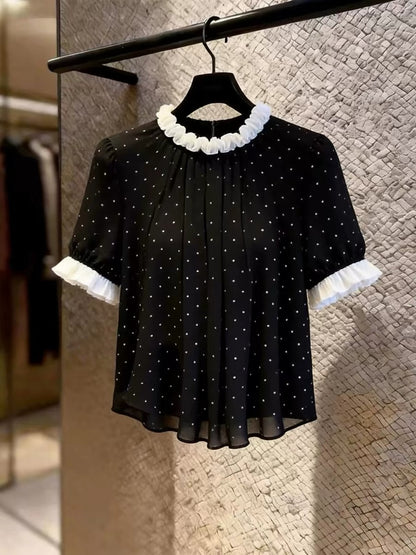 Women's black short-sleeved top featuring a stylish, unique design with a ruffled collar and polka-dot print; a chic, versatile, and flattering piece perfect for layering or wearing on its own in summer.